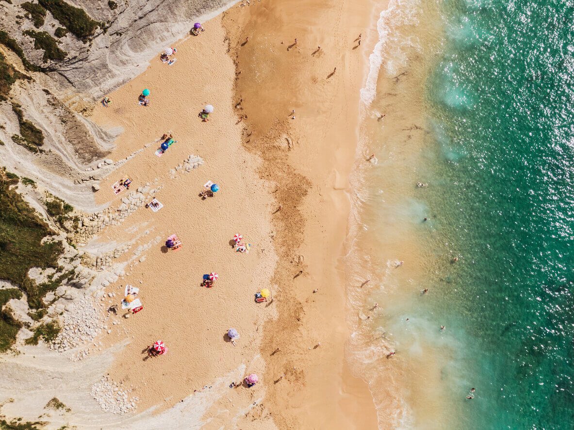 A beach in summer with a large amount of people, but who maintain social distancing measures beacuse of the Coronavirus COVID-19 outbreak. The image has been digitally modified to show a distance between people, towels, umbrellas, longer than 1.5 meters (5 feet).